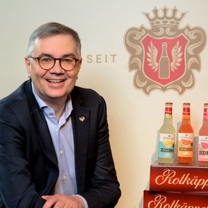 Christof Queisser sitzend vor dem Rotkäppchen-Logo, neben ihm das Neuprodukt Secconade