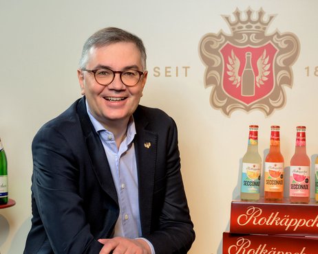 Christof Queisser sitzend vor dem Rotkäppchen-Logo, neben ihm das Neuprodukt Secconade