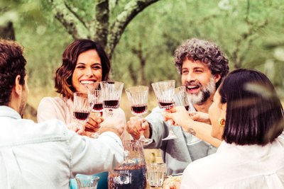 Vier Personen sitzen an einem Tisch am Waldrand und stoßen mit Rotwein an