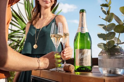 Zwei Frauen stehen bei strahlendem Sonnenschein auf einem Balkon und trinken Mumm